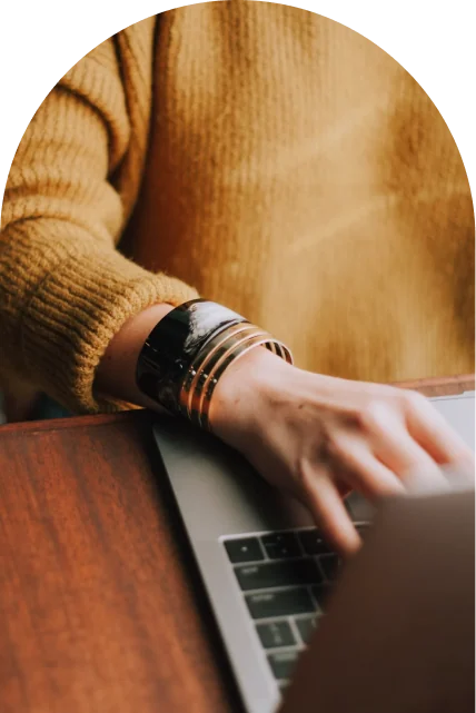 Close up of a person in a mustard jumper typing on a laptop