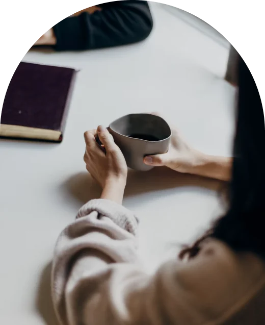 Two people sitting at a table, one holding a cup of coffee